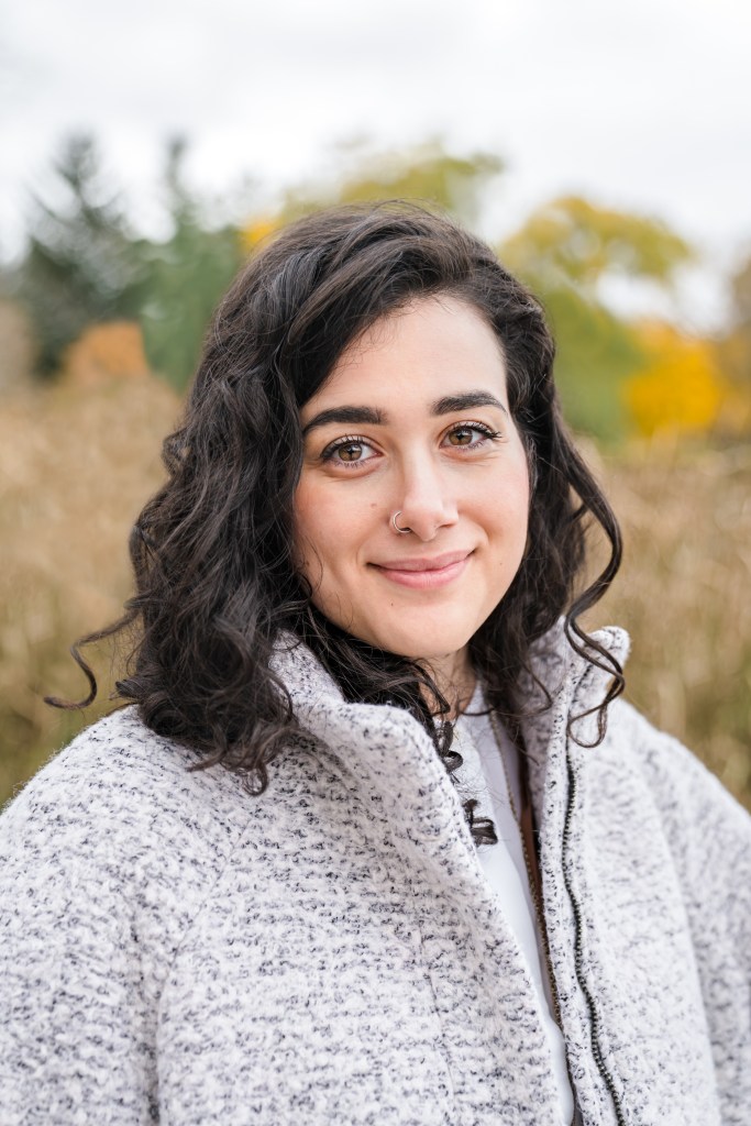 A portrait photograph of Tara Farahani, against a natural background of fall colours.